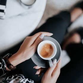 business woman sits next to a marble table with books and holds a saucer with a cup of espresso