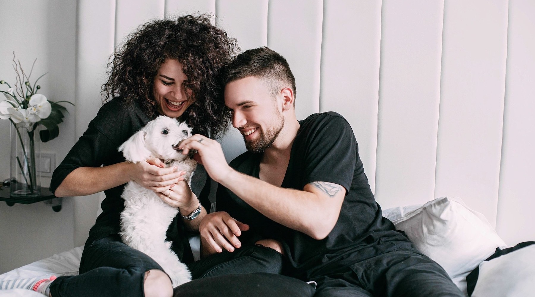 a man and woman sitting on a bed playing with a dog